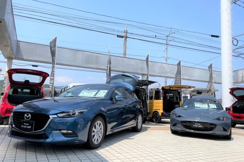 県道沿いには、デミオ（MAZDA2）やロードスターの中古車を並べています。